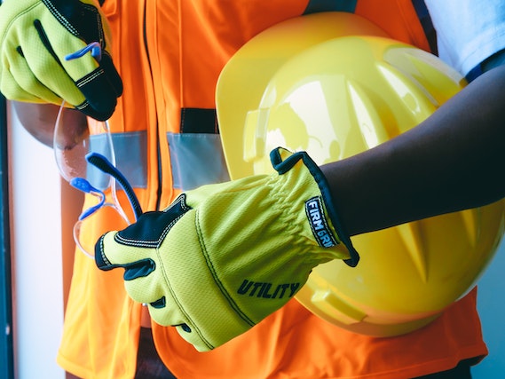 maintenance worker in orange reflective vest and green gloves holding a yellow hardhat